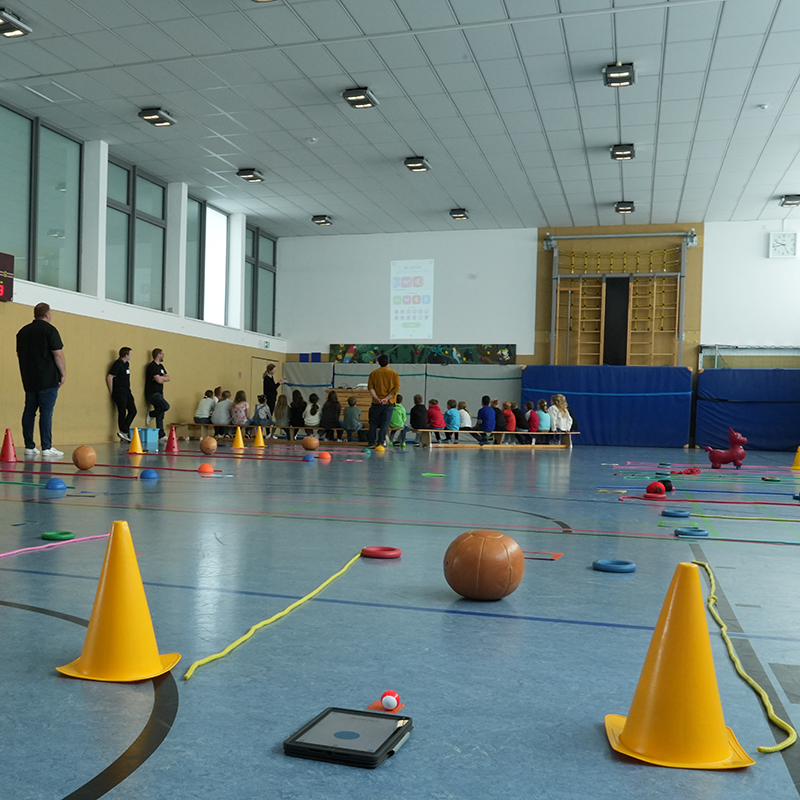 Aktion Codekids in Turnhalle einer Schule – Kinder programmieren kleine Bälle und absolvieren damit einen Geschicklichkeitsparcours mit Hinternissen